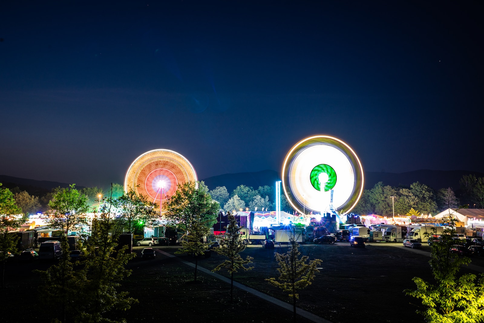 a fairground at night with a ferris wheel in the foreground
